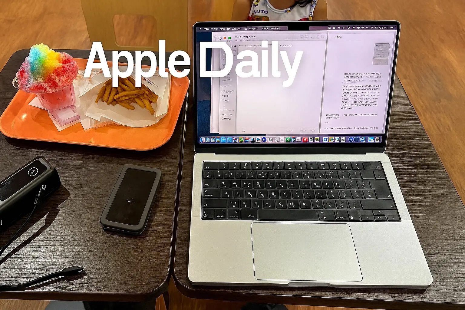 MacBook on a food court table at Tokyo Tower with rainbow shaved ice, French fries, and a portable battery, representing Apple Daily #9 work and lifestyle scene.