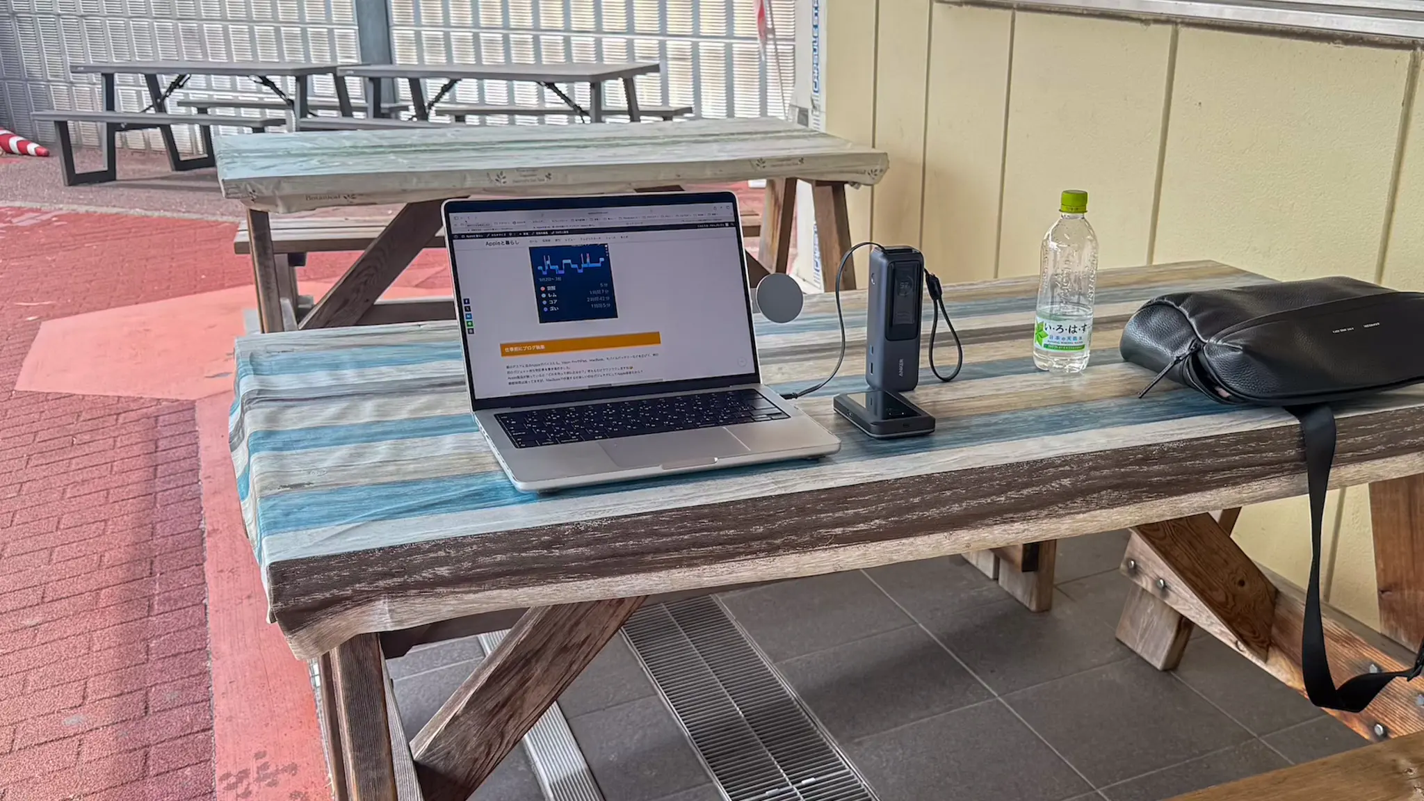 外のテーブルでMacBookを広げ、モバイルルーターとバッテリーを使って作業中のApple日常